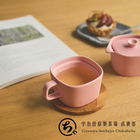 木桌上擺放著粉色方形美濃燒馬克杯與茶壺，杯中盛裝著茶飲，後方有一本雜誌與點心，右下方印有宇治田原製茶場直賣部的品牌標誌。