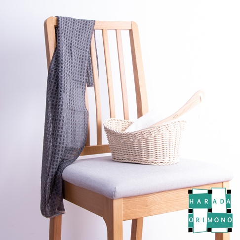 淺灰色網格紋沐浴巾搭在木椅上，椅上擺放著一個藤編籃，籃內有一條白色毛巾和一個木柄。