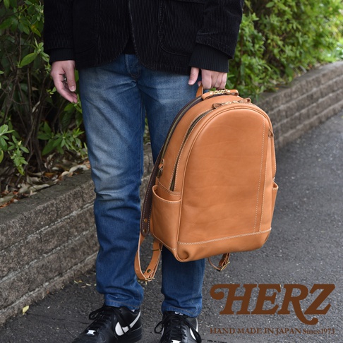 職人手作皮革多功能後背包 R-21，採用溫暖的棕褐色皮革，設有雙拉鍊主隔層、側邊口袋和可調節皮革背帶，整體設計簡約實用。