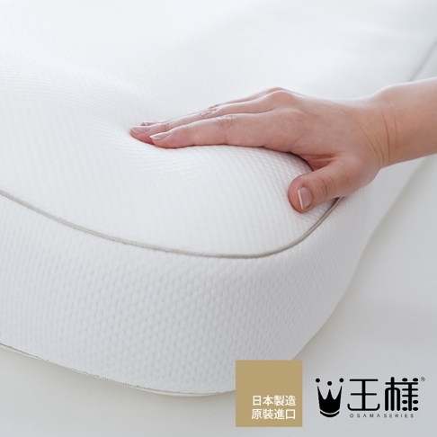 白色枕套，表面有細緻的紋理，邊緣有淺灰色滾邊。一隻手輕壓在枕套上，展示其柔軟度。角落有「日本製造 原裝進口」字樣及品牌Logo。