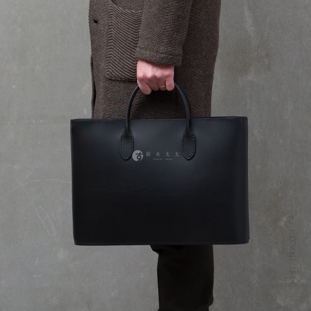 黑色職人手作皮革Organ薄型公事包，簡約設計，配有皮革提把，包款中央有燙金Logo，整體風格俐落。