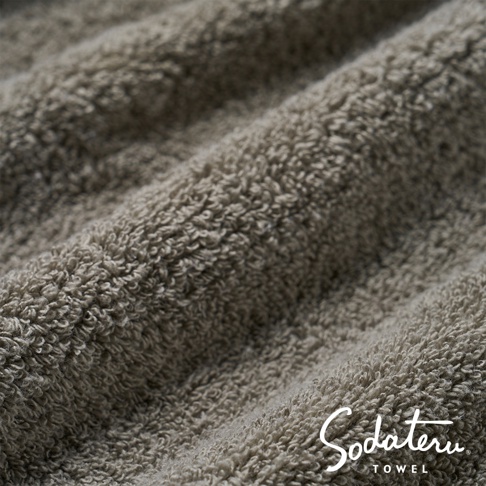 feel 輕蓬快乾恆柔雲感浴巾，特寫畫面展示其細膩蓬鬆的織紋，呈現柔和的灰褐色調，質地觸感極佳。