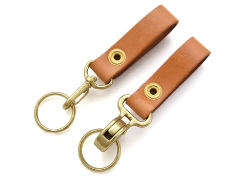 兩個職人手作皮革鉤扣鑰匙圈，顏色為淺棕色，材質為皮革，配有黃銅色金屬鉤扣、固定環和鑰匙圈。