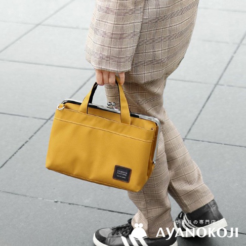 一位女士提著一個黃色的口金手提包，穿著格紋褲裝和運動鞋