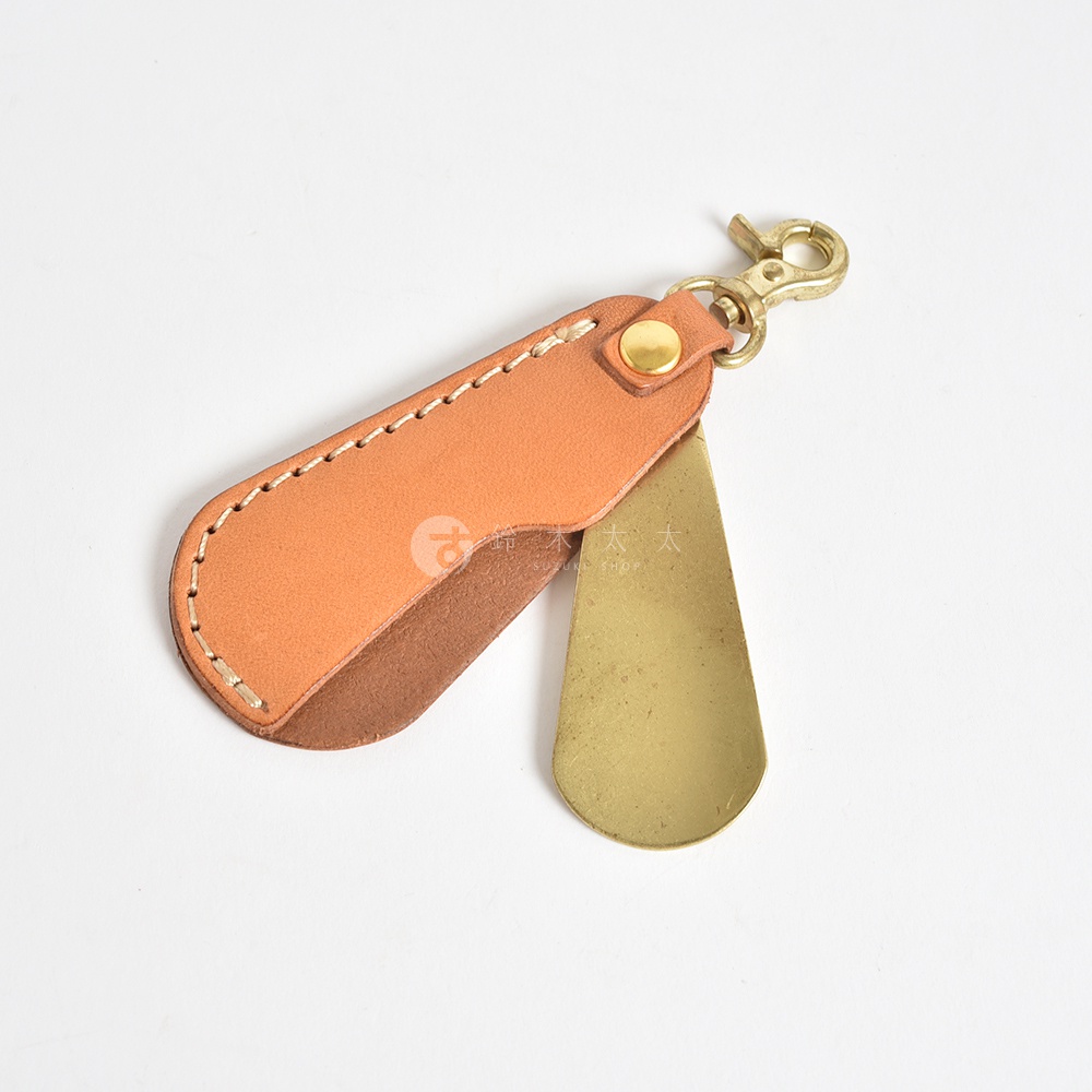職人手作皮革隨身金屬鞋拔，皮革部分為淺棕色，搭配黃銅色金屬鞋拔，以車縫線固定，並附有黃銅色掛鉤。