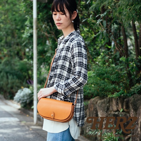 職人手作的皮革迷你馬鞍包，採用溫潤的焦糖棕色皮革，包身呈半月形，配有可調節的長肩帶，包蓋上有一顆小巧的旋鈕式鎖扣。