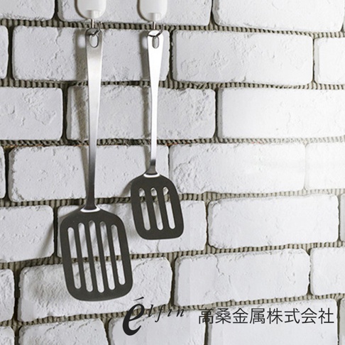 日製不鏽鋼輕薄煎匙 (大)，銀色，一組兩個，帶有圓孔掛柄，鍋鏟部分為長方形，邊緣為圓角，表面有長條狀鏤空設計，方便瀝油，以白色磚牆為背景。