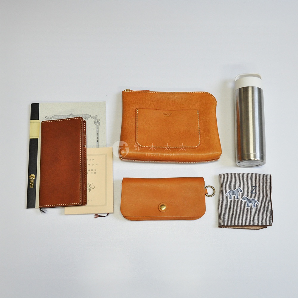 多個皮革配件，包含一個棕色長夾、一個棕色手拿包、一個淺棕色筆記本、一個銀色保溫瓶，以及一條印有斑馬圖案的條紋手帕。