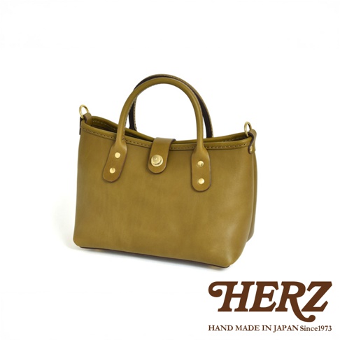 一咖橄欖綠色、職人手作的迷你皮革托特包，包身呈現自然皮革紋理，配有圓潤提把，中央以金屬釦開合，兩側飾有黃銅鉚釘。