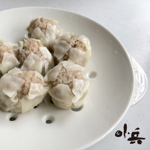 白色陶瓷美濃燒多用蒸盤上，擺放著六顆剛蒸熟的燒賣，內餡為豬絞肉，外皮為白色麵皮，蒸氣繚繞。