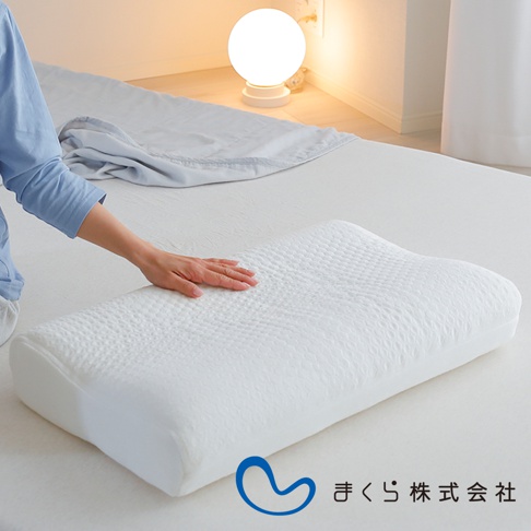 白色人體工學枕，表面有蜂巢狀紋理，枕套材質為透氣織物，一隻手輕柔地放在枕頭上，背景是臥室環境，有檯燈和床鋪。