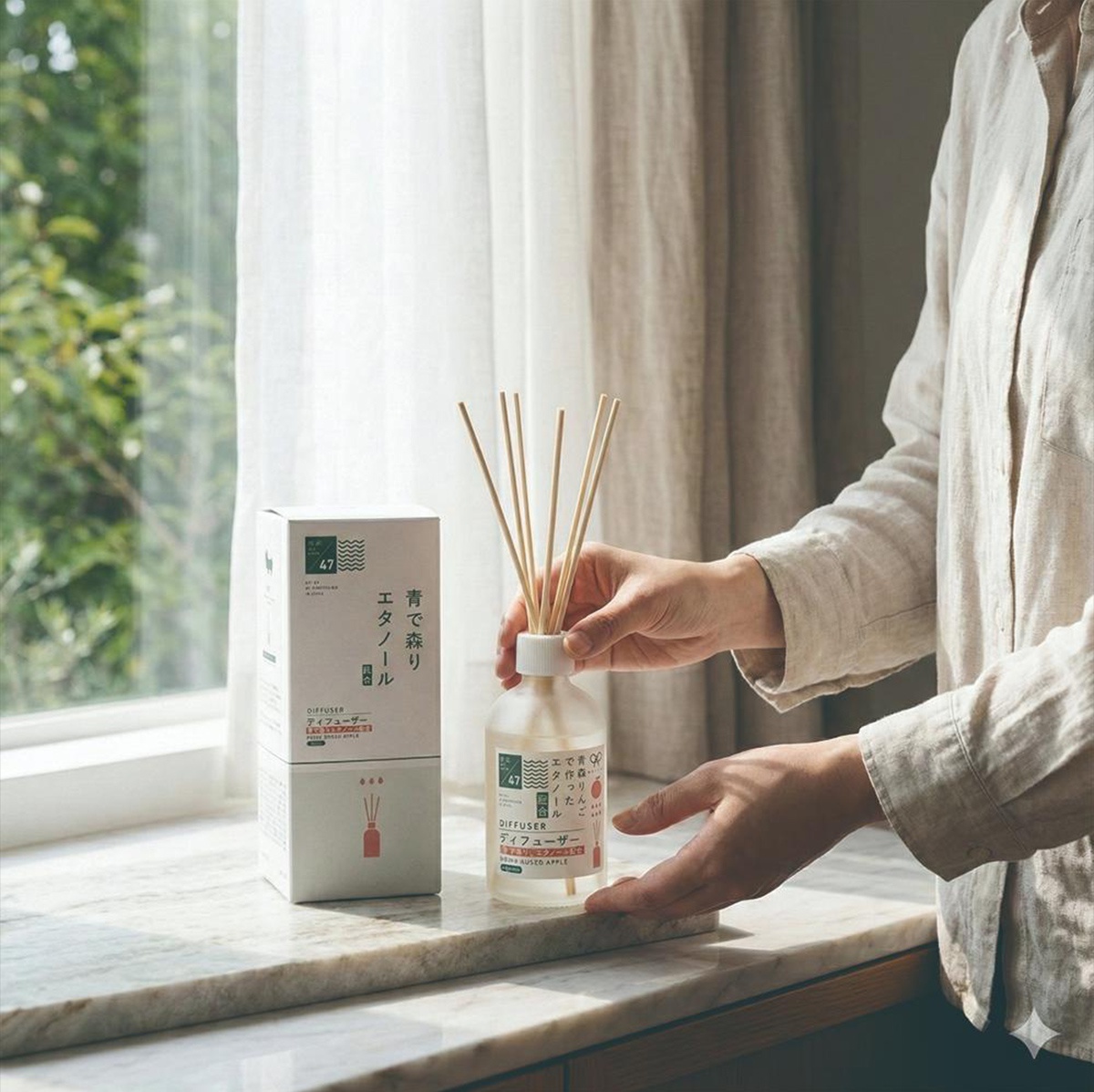 一個女人拿著一款帶有擴香竹的青森蘋果香氛擴香瓶，旁邊有一個同款香氛的盒子。