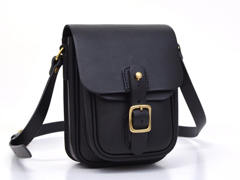 黑色皮革直式單肩包，配有金色皮扣和可調節肩帶。