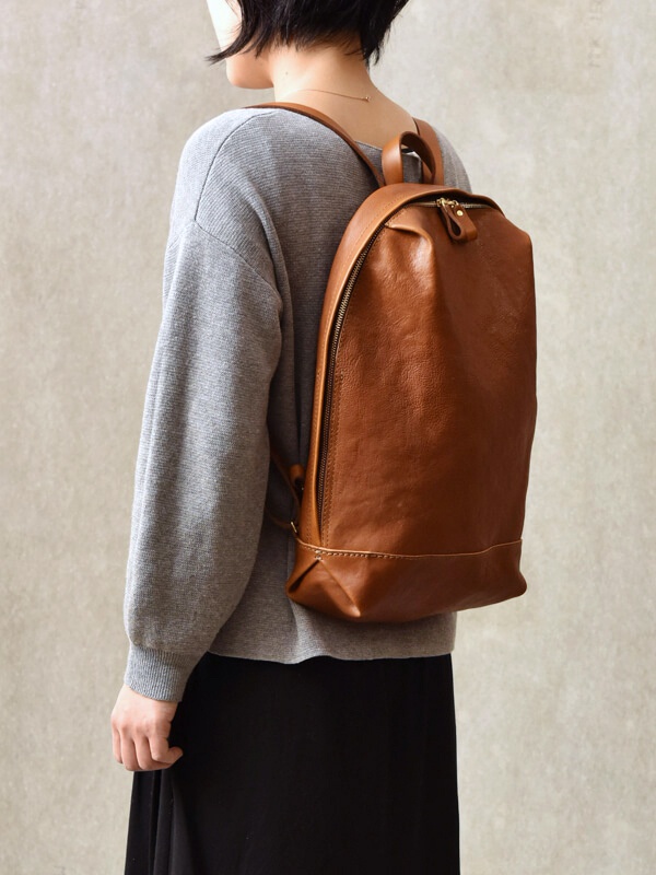 棕色皮革後背包，設有拉鍊開口和皮革拉環，背包側面有品牌標誌。