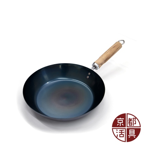 一個28公分、深藍色的圓形平底鐵鍋，鍋身呈現均勻的熱處理藍色調，配有木質手柄，手柄末端有一個金屬掛環。