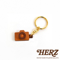 職人手作皮革相機造型鑰匙圈，咖啡色皮革製成，搭配深棕色鏡頭細節，配有金色金屬環與扣環。