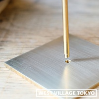 黃銅圓柱狀燈架與銀色金屬方形底座，底座表面有細緻的髮絲紋，圓柱底部有螺紋，對應底座上的螺孔，準備組裝。