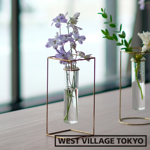黃銅四角玻璃花器，內置玻璃試管，盛有淺紫色花朵與綠葉，整體為簡約現代風格。