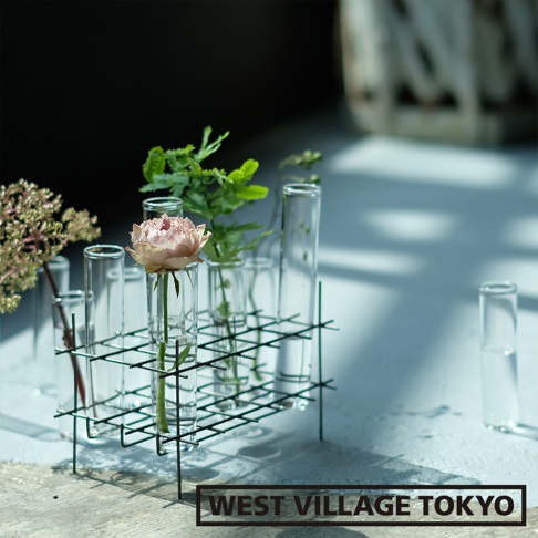 多格一輪玻璃花器，黑色金屬網架支撐多個玻璃試管，其中一支試管插有一朵粉色玫瑰，另有綠葉植物點綴。