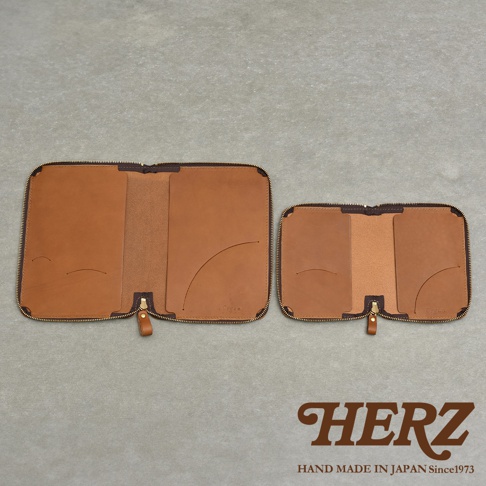 兩個皮革記事本收納包，一個較大，一個較小，皆為棕褐色，採用拉鍊開合設計，內有卡槽和筆槽，下方有HERZ品牌標誌。
