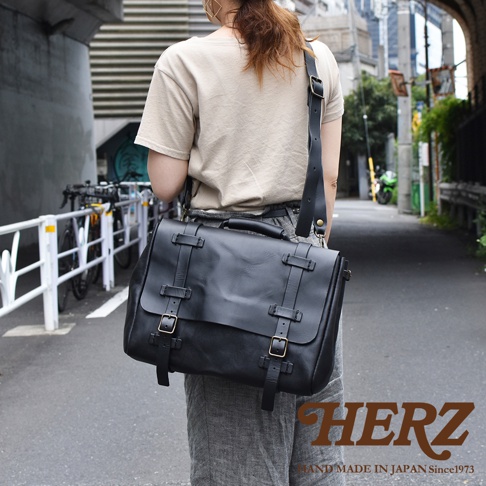 黑色皮革復古郵差包，配有雙搭扣和可調節肩帶，由職人手工製作。