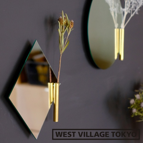 菱形鏡面壁掛花器，搭配金色金屬管狀花筒，內插乾燥植物，背景為深色牆面。