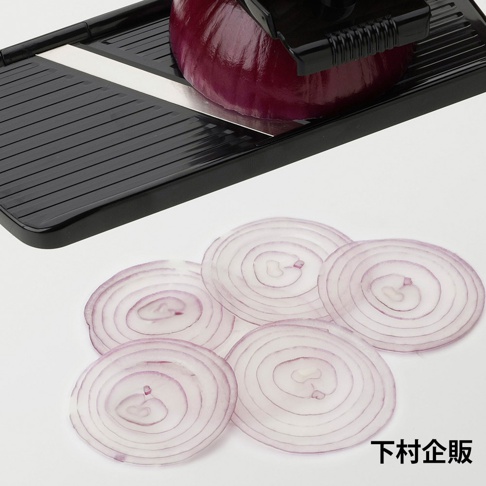 黑色塑膠製的四合一刨絲器，刨出數片紫洋蔥圈，呈現同心圓紋理。