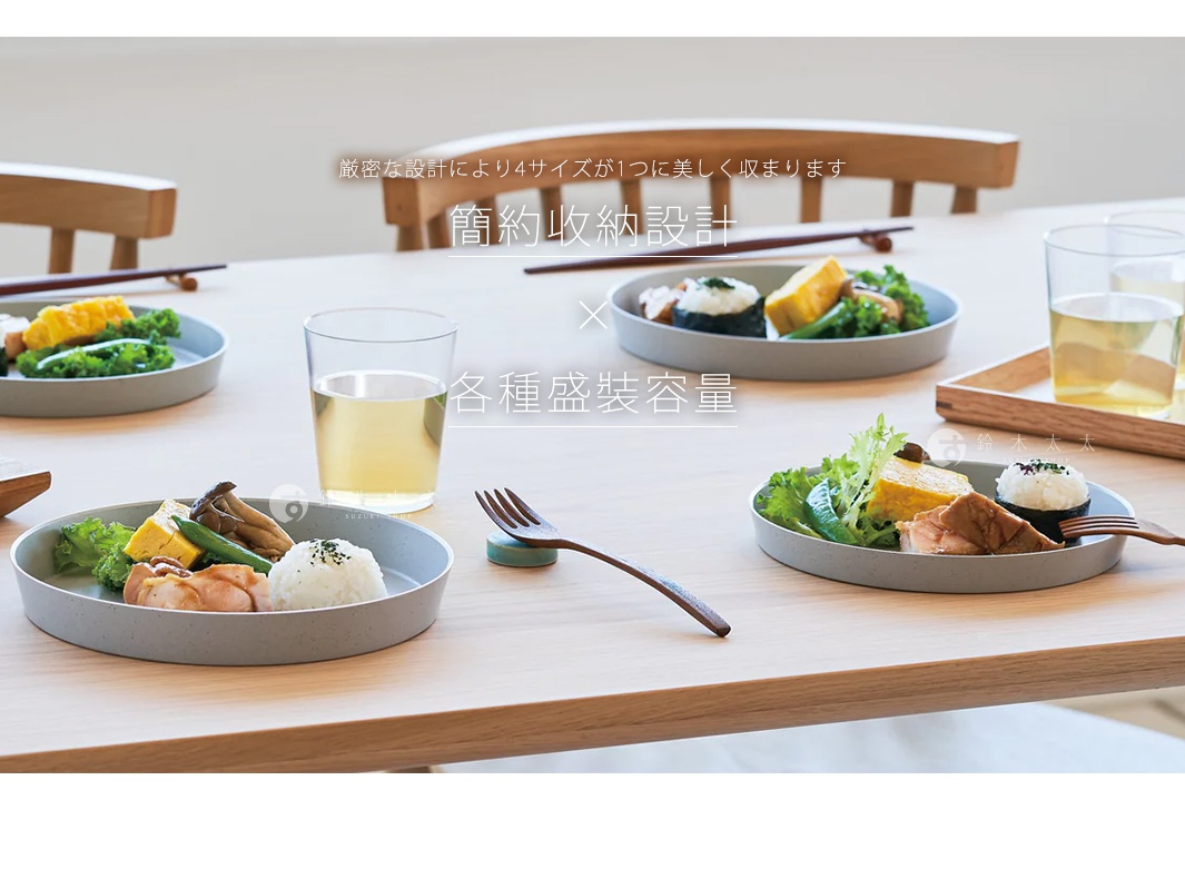 FIT DISH 安全防摔餐盤，灰色，材質看似塑膠或密胺，設有淺邊緣，盛有日式料理、米飯、蔬菜和肉類，搭配玻璃杯和餐具，擺放在木質餐桌上。