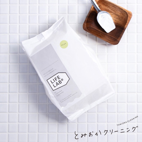 白色補充包，印有「LIFE LAB。」標誌和日文文字。旁邊有一個小木碗，內有一銀色勺子，勺子裝有白色粉末。背景是白色馬賽克瓷磚。