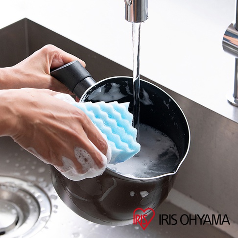 手持深棕色鑽石不沾單柄小湯鍋，用藍色海綿於水槽中清洗，鍋內有泡沫。