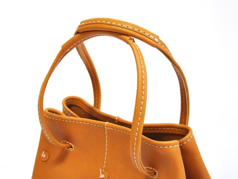 淺棕色皮革托特包，特寫展示包包的提把和邊緣縫線，以及側邊的抽繩設計。