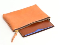 一個淺棕色皮革製的存摺文件收納夾，拉鍊為深棕色，附有金屬拉鍊頭和同色皮革拉環。收納夾內可見部分藍色圖案的內襯。