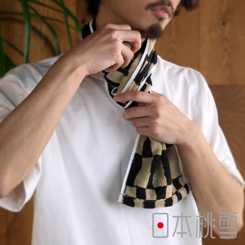 穿著白色T恤的人正在將一條淺棕色和黑色格紋的毛巾圍在脖子上，毛巾邊緣有白色條紋。