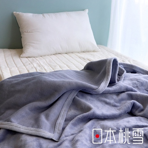 舒眠雙面四季毯，呈現柔和的淺紫色絨毛材質，毯邊有細緻的滾邊。背景為白色床墊與白色枕頭，整體營造溫馨舒適的睡眠氛圍。