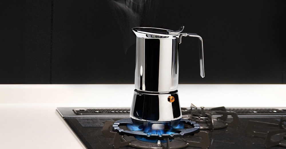 全不鏽鋼摩卡壺，置於黑色爐架上，爐架下方有藍色火焰。摩卡壺頂部有蒸氣冒出。