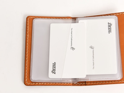 職人手作皮革卡片收納夾，卡其色牛皮材質，內含多個透明卡槽，並有品牌「HERZ」及「The Heart of Craftsmanship」字樣壓印。