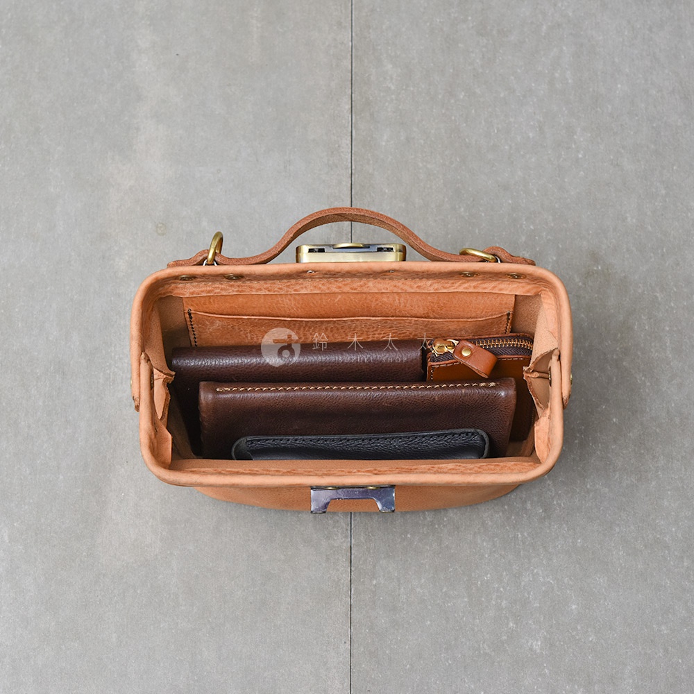 一駝色皮革製的醫生包，內有深棕色、淺棕色和黑色皮夾，包包為頂視角拍攝，背景為灰色水泥牆