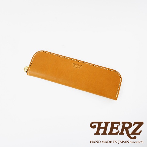 駝色皮革筆袋，頂部壓印有HERZ品牌字樣和MADE IN JAPAN字樣，縫線細緻，側邊有金色拉鍊頭。