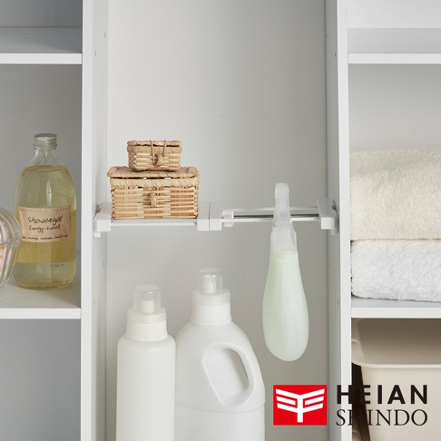層架上擺放著兩罐不同大小的洗劑，以及一組疊放的草編收納盒，一個噴霧瓶懸掛在伸縮架上，右側疊放著兩條毛巾，底部有收納盒。