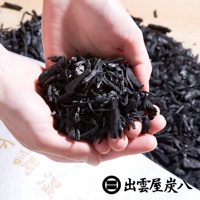 一雙手捧著黑色的碎木炭，背景是堆積的木炭。