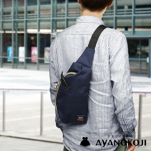 一名男子背著海軍藍的 AYANOKOJI Sarei 機能布水滴型口金斜背包，包包斜背在身前，展示了其獨特的造型與設計。