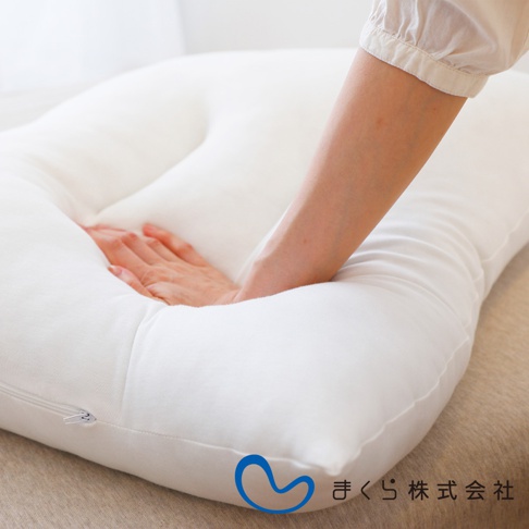 一張白色無敵軟枕，枕套為純棉材質，帶有拉鍊。一隻手壓在枕頭上，展示其柔軟度。