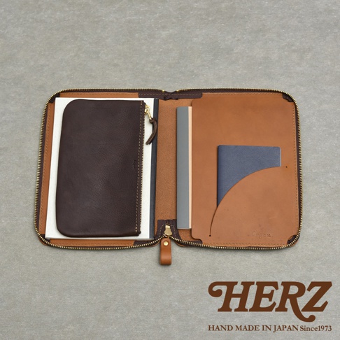 一個打開的棕色皮革記事本收納包，內部有幾個隔層，包含一個深棕色拉鍊小包、一本灰色的筆記本和一本藍色的護照。