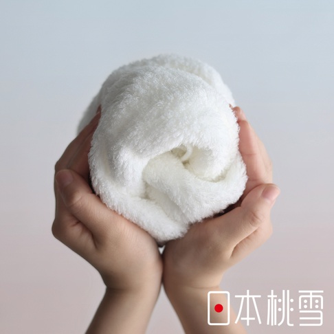 一雙手捧著一團蓬鬆柔軟的白色毛巾，右下角有日本桃雪的標誌和文字。