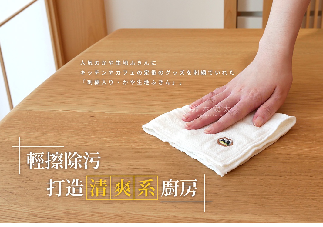 一隻手拿著白色八重紗精繡萬用吸水擦拭巾，擦拭木質桌面。擦拭巾有精緻的繡花圖案。