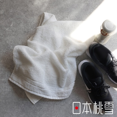 白色 Lite! 輕生活快適速乾薄手迷你浴巾，柔軟材質，搭配黑色運動鞋和白色水壺，背景為灰色水泥紋理。