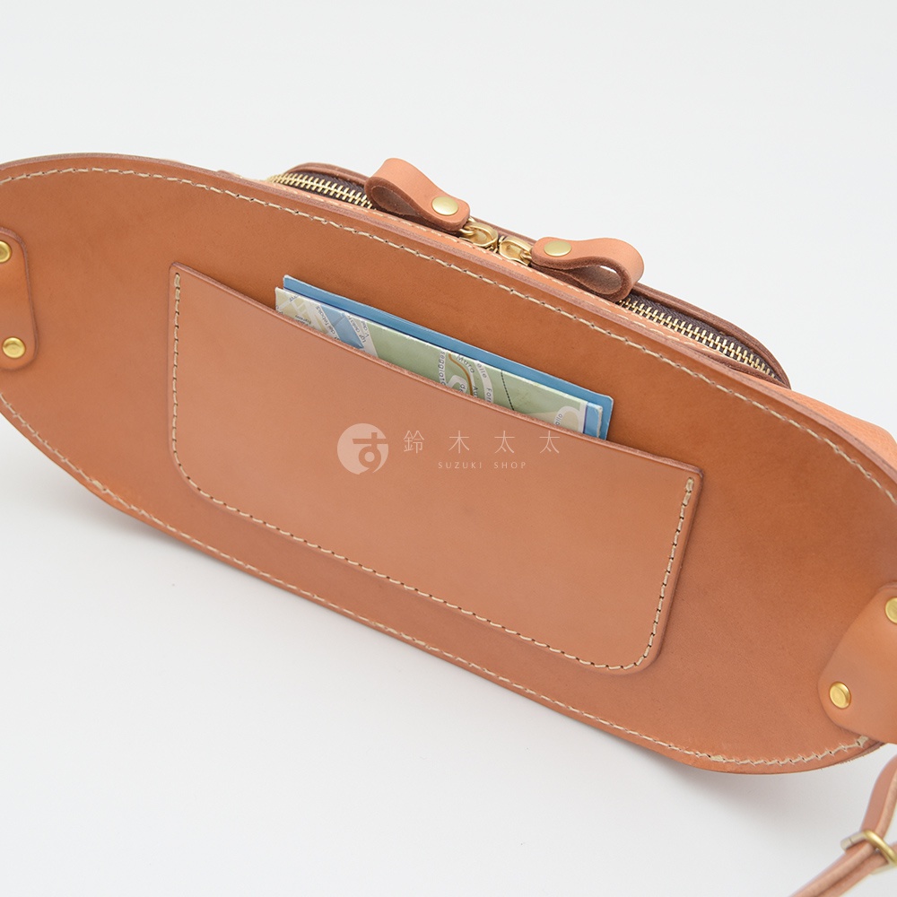日本HERZ職人手作皮革拉鍊旅行斜背包 F-7，展示了棕色皮革材質，主體為斜背包，特寫其背面口袋，內有卡片，印有SUZUKI SHOP字樣