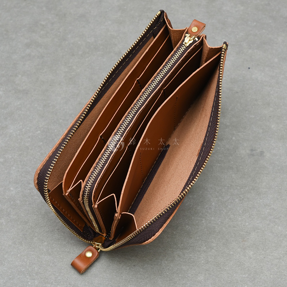 一個棕色皮革拉鍊長夾，內部有許多隔層，拉鍊為金色，夾子為棕色皮革製成，上面有一個圓形金屬鈕扣。