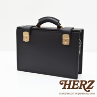 黑色皮革兩用機師箱，配有金色鎖扣及提把，簡約設計，展現職人手作質感。