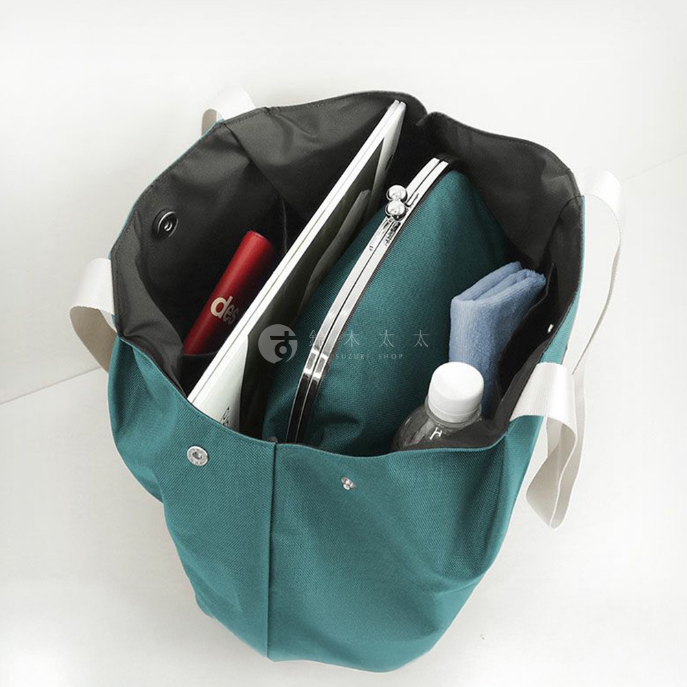 一窺 AYANOKOJI 機能布兩用托特包的內部，可見一支紅色唇膏、一個平板電腦，以及一個綠色手拿包，一旁還有摺疊的淺藍色毛巾和一瓶水。